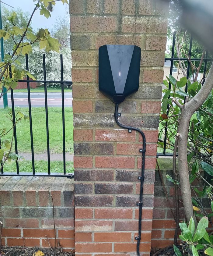 Black EV charger mounted on a brick gate pillar